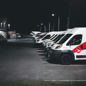 A lineup of white and red delivery vans parked in a lot under streetlights at night.