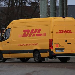 Yellow DHL van on street showing company branding and delivery services.